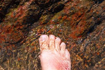 Close-up of a foot under water on stony ground on the beach. Cooling wet for sunburn.
