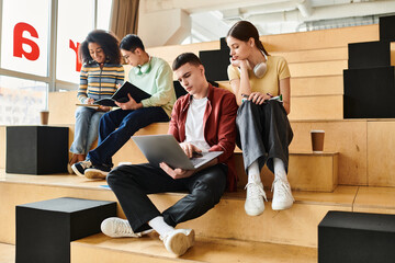 A multicultural group of students sit on steps, working together on a laptop in an educational setting.