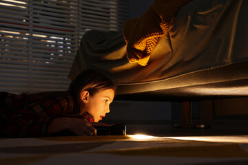 Obraz na płótnie Canvas Little girl with flashlight looking for monster under bed at night