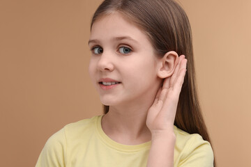 Little girl with hearing problem on pale brown background