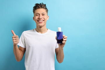 Young man with mouthwash showing thumbs up on light blue background, space for text