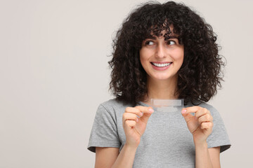 Young woman holding teeth whitening strips on light grey background, space for text