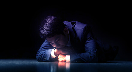 失敗し暗い部屋で跪き項垂れ絶望するスーツを着た仕事中のビジネスマンの日本人男性　後悔・謝罪・増税・落ち込む・鬱・破産のイメージ