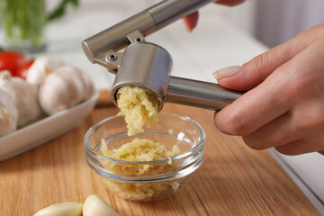 Woman squeezing garlic with press at wooden table, closeup - obrazy, fototapety, plakaty