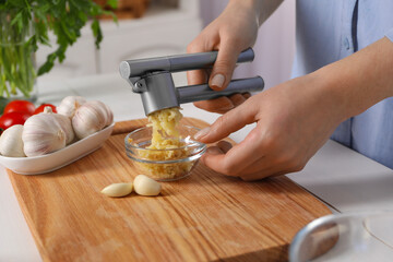 Woman squeezing garlic with press at white wooden table, closeup