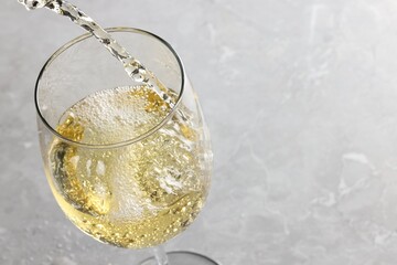 Pouring tasty aromatic wine in glass at gray marble table, closeup. Space for text