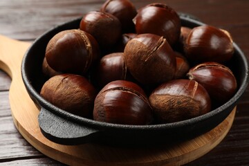 Roasted edible sweet chestnuts in baking dish on wooden table, closeup