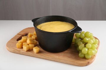 Fondue with tasty melted cheese and grapes on white table