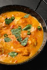 Tasty chicken curry with parsley and pepper on black table