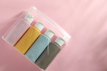 Cosmetic travel kit in plastic bag on pink background, top view. Space for text