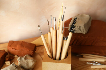 Clay and set of modeling tools on wooden table in workshop, closeup