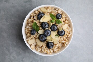 Tasty oatmeal with blueberries, mint and almond petals in bowl on grey table, top view