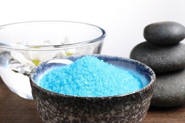Obraz na płótnie Canvas Light blue sea salt in bowl, spa stones and flowers on table against white background, closeup