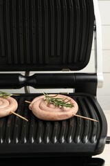 Electric grill with homemade sausages and rosemary on light background, closeup