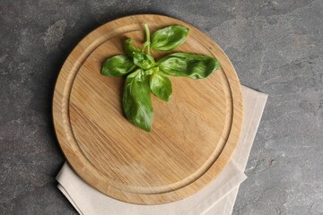 Wooden cutting board, fresh basil and napkin on grey table, top view
