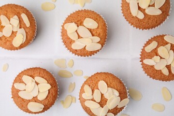 Muffins with fresh almond flakes on white tiled table, flat lay