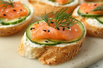 Tasty canapes with salmon, cucumber and cream cheese on table, closeup