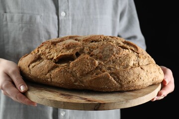 Woman holding freshly baked bread on black background, closeup