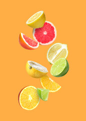 Many different fresh citrus fruits falling on orange background