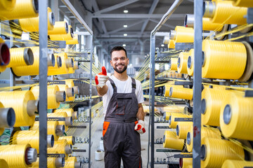 Textile factory worker holding thumbs up by industrial knitting machine.