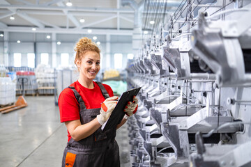 Portrait of female factory worker holding checklist and standing by production line machine.