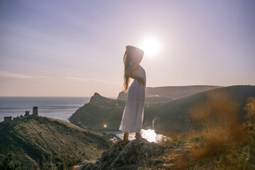 woman stands on a hill overlooking the ocean, her arms raised in the air. Concept of freedom and joy, as if the woman is celebrating a moment of happiness or accomplishment.