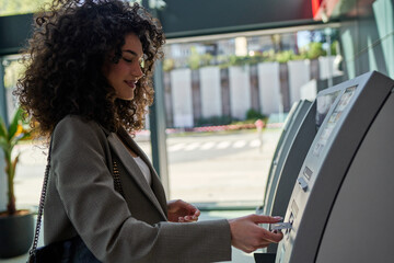 Elegant woman with a chic blazer using a street-side ATM, urban life in the background.