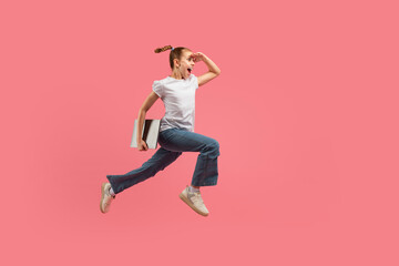 Energetic kid jumping with books against pink
