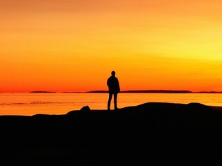 Fototapeta na wymiar man standing on beach looking out to sea at sunset, from rocks in foreground