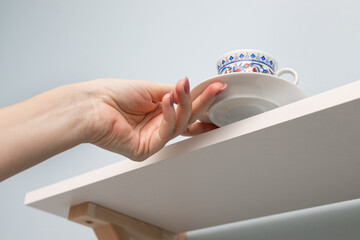 a woman's hand removes coffee utensils from the kitchen shelf.