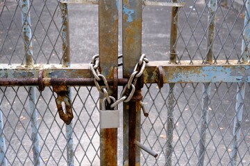 Rusty iron door with mesh fences locked with a new metal chain and a padlock