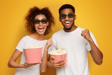 Laughing couple in 3d glasses holding buckets of popcorn