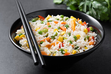 White rice with vegetables in a black bowl on black background