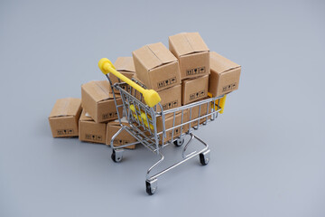 Shopping cart and many carton boxes on gray background. Buying and shipping concept.