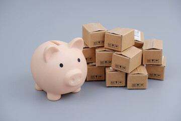 Save money for shipping concept. Many carton boxes and piggy bank on gray background.