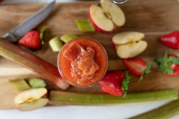 Fresh rhubarb compote  cooked with strawberries in apples in a glass jar from above on a cutting board with ingredients