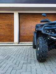Vertical shot of a quad bike parked outside of a garage with a wooden gate © Wirestock