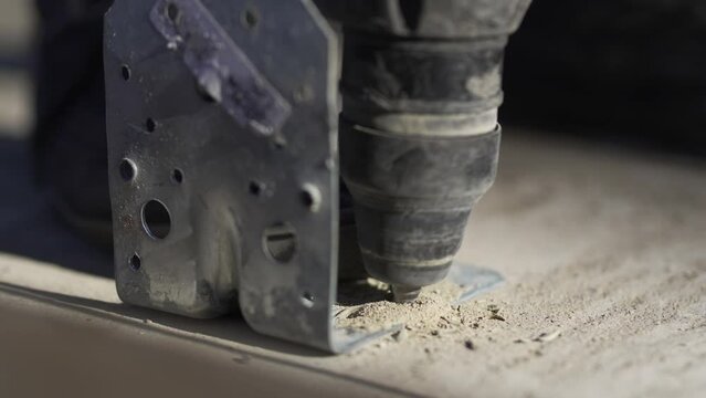 Worker uses perforator and coach bolt to connect angle beam to concrete beam. Construction activity unfolds dynamically in workshop