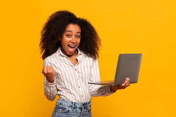 Excited woman holding laptop with fist pump