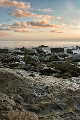 Vertical shot of a beach full of rocks with a calm sea in the background in the evening