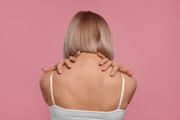 Woman suffering from pain in her neck on pink background, back view