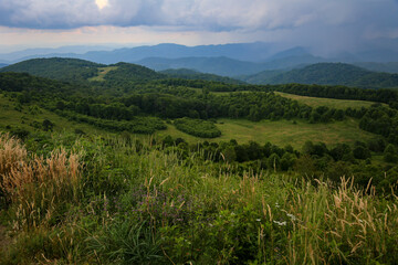 Beautiful top view of the mountain range covered with forest, with a cloudy sky in the background