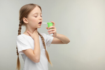 Little girl using throat spray on light grey background. Space for text