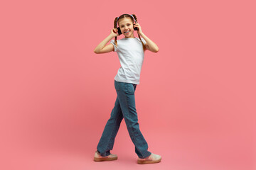 Girl walking and listening to music on pink
