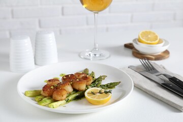 Delicious fried scallops with asparagus, lemon and thyme served on white table