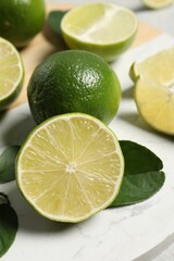 Fresh ripe limes and leaves on table, closeup