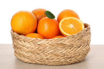 Fresh oranges in wicker basket on light wooden table against white background