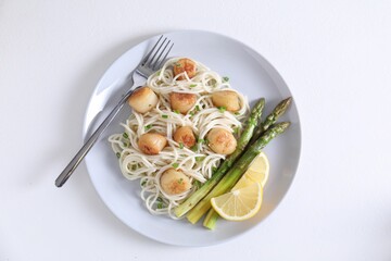 Delicious scallop pasta with asparagus, green onion and lemon served on white table, top view