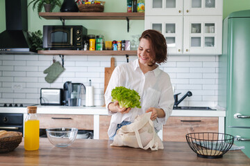 Caucasian cheerful young woman preparing salad while standing in the kitchen at home