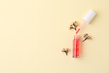 Bright lip gloss, applicator and flowers on yellow background, top view. Space for text
